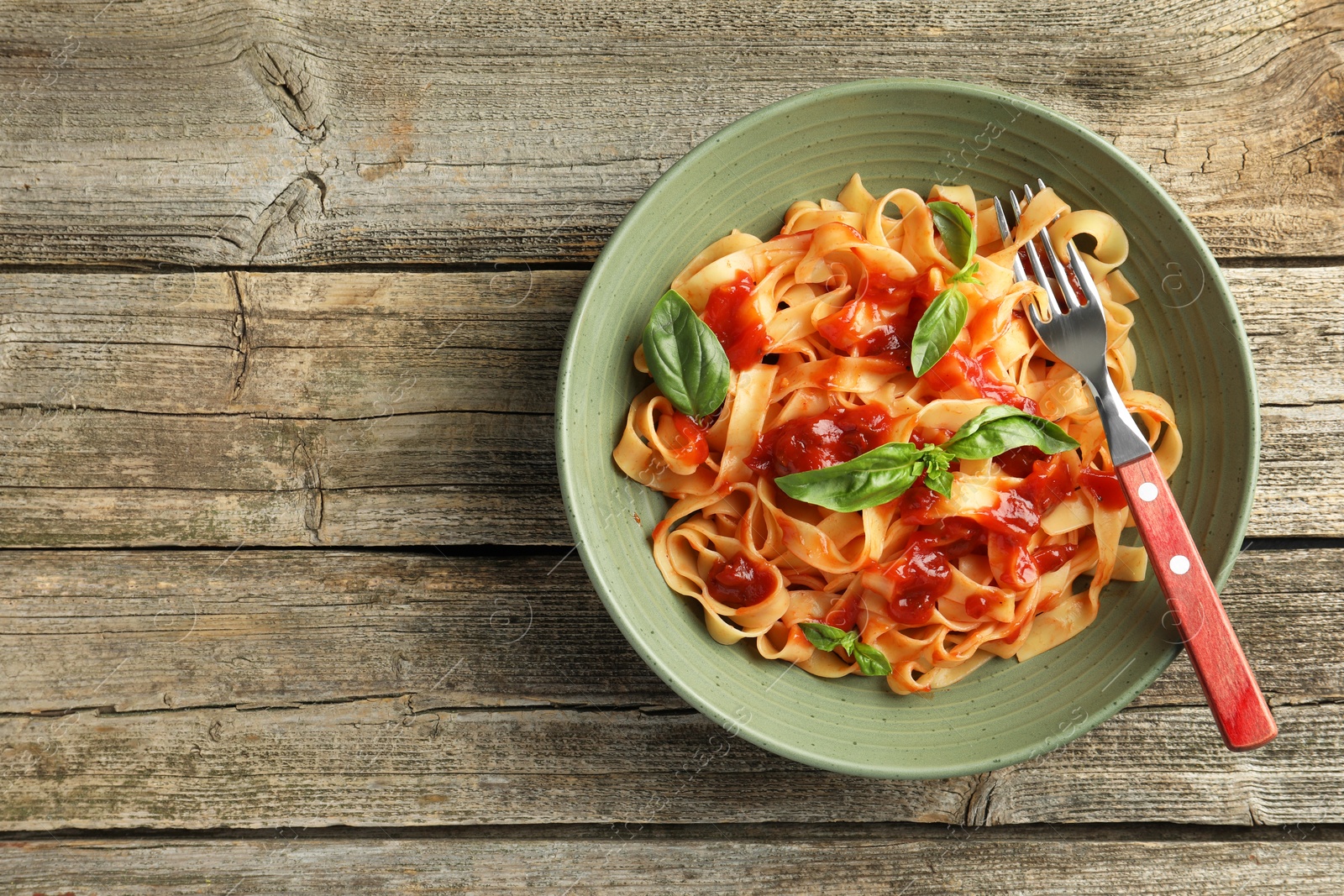 Photo of Delicious pasta with tomato sauce and basil in bowl on wooden table, top view. Space for text