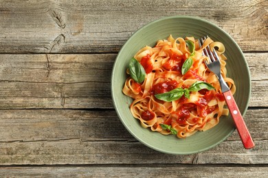 Photo of Delicious pasta with tomato sauce and basil in bowl on wooden table, top view. Space for text