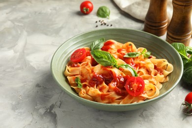 Photo of Delicious pasta with tomato sauce and basil in bowl on grey textured table, closeup. Space for text