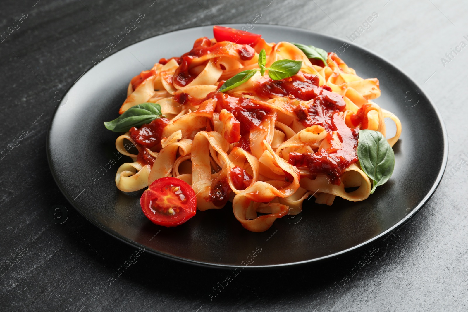 Photo of Delicious pasta with tomato sauce, vegetable and basil on dark textured table, closeup