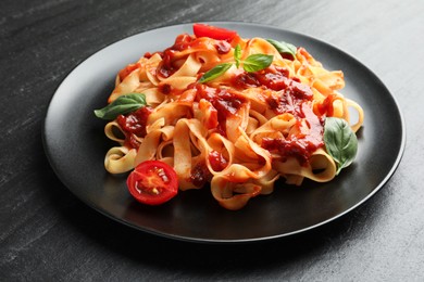 Delicious pasta with tomato sauce, vegetable and basil on dark textured table, closeup