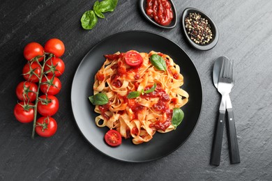 Photo of Delicious pasta with tomato sauce, vegetable, basil and spices served on dark textured table, flat lay