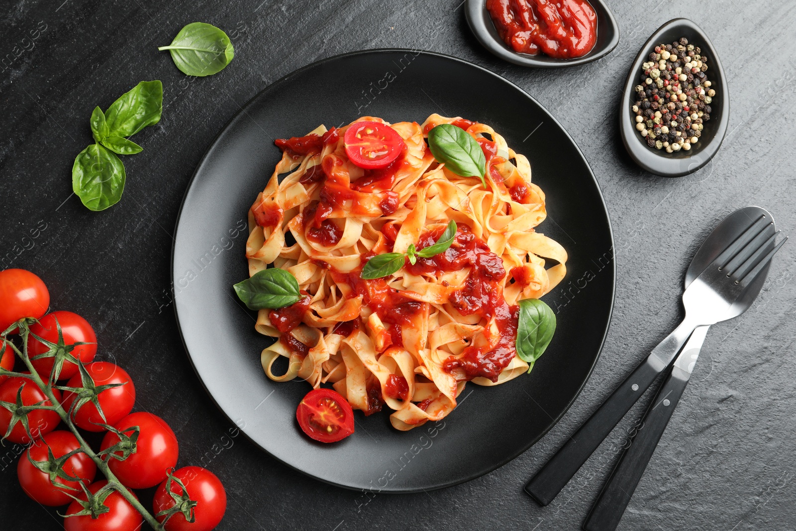 Photo of Delicious pasta with tomato sauce, vegetable, basil and spices served on dark textured table, flat lay