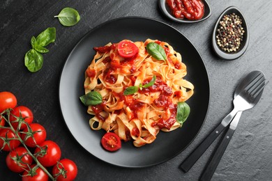 Delicious pasta with tomato sauce, vegetable, basil and spices served on dark textured table, flat lay