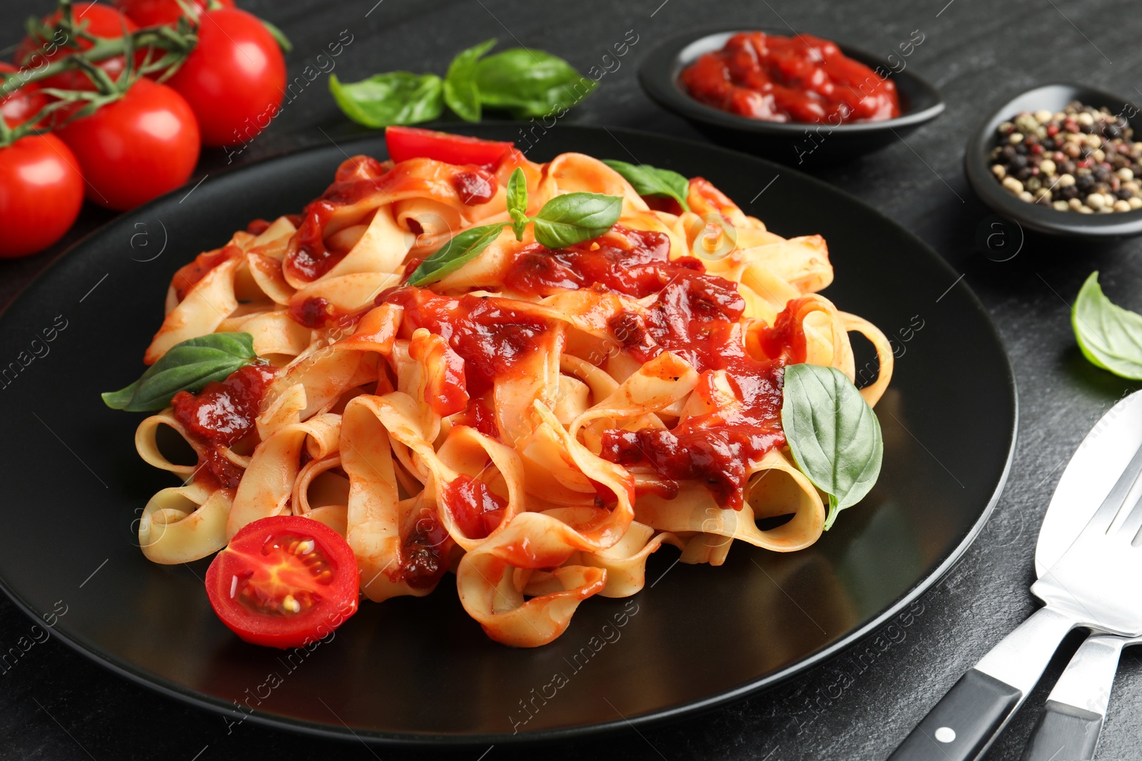 Photo of Delicious pasta with tomato sauce, vegetable, basil and spices served on dark textured table, closeup