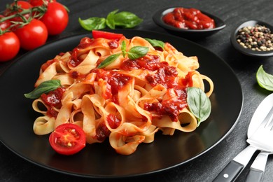 Photo of Delicious pasta with tomato sauce, vegetable, basil and spices served on dark textured table, closeup