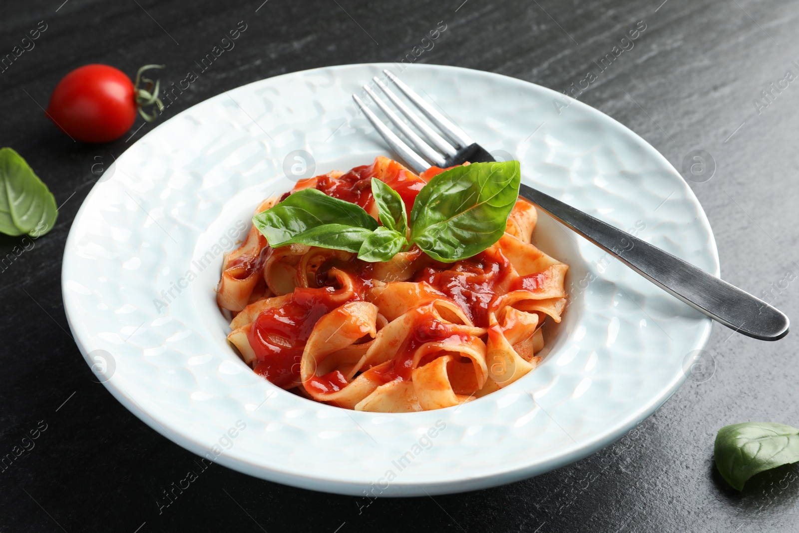 Photo of Delicious pasta with tomato sauce and basil on dark textured table, closeup