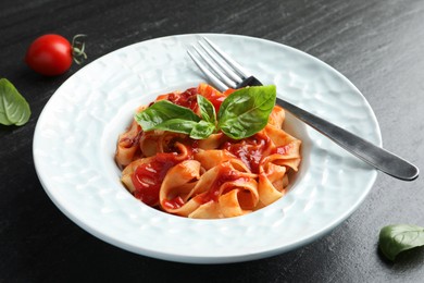 Delicious pasta with tomato sauce and basil on dark textured table, closeup