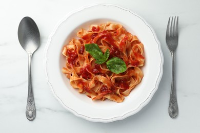 Photo of Delicious pasta with tomato sauce and basil served on white marble table, flat lay