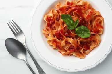 Photo of Delicious pasta with tomato sauce and basil served on white marble table, flat lay