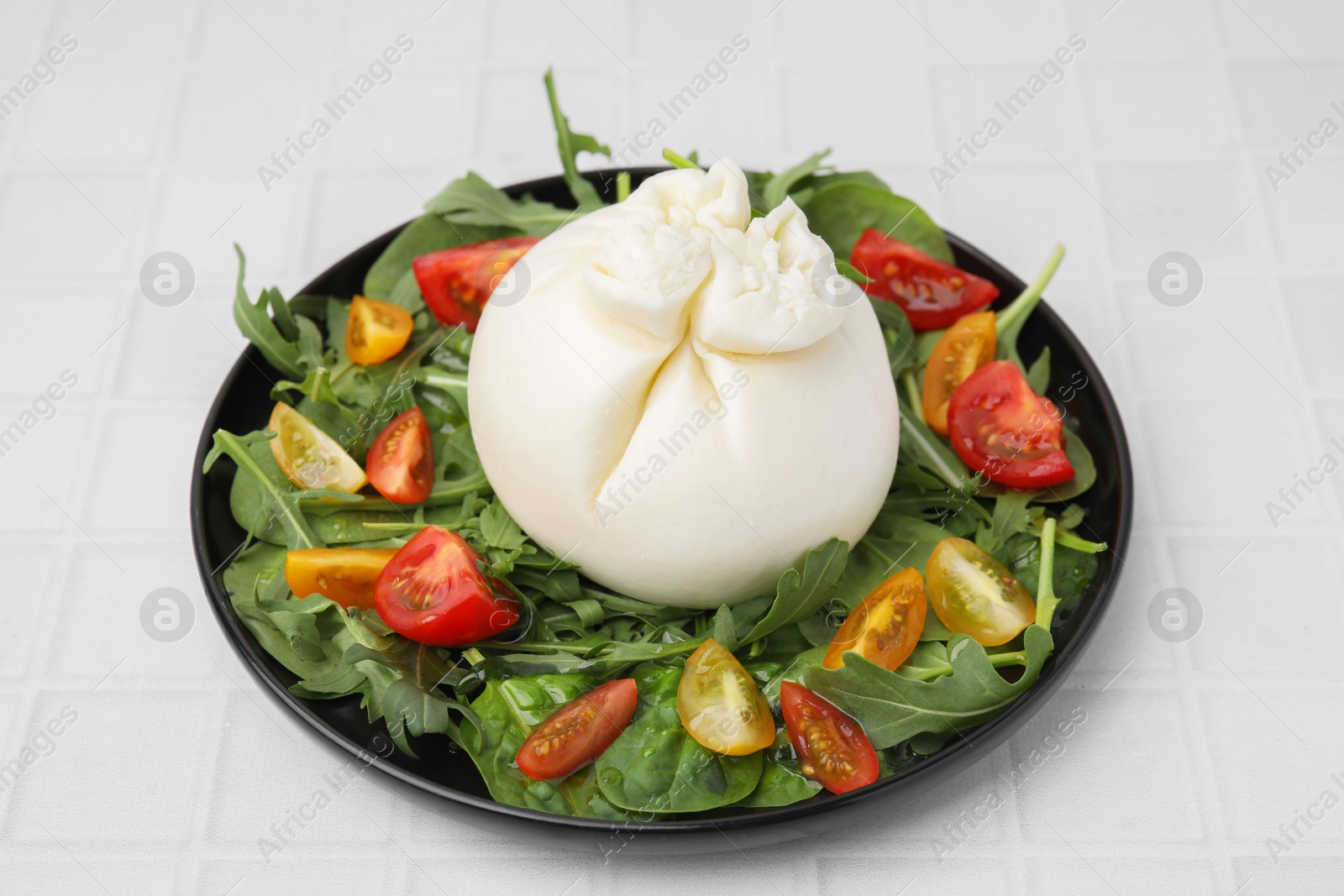 Photo of Delicious burrata salad on white tiled table, closeup