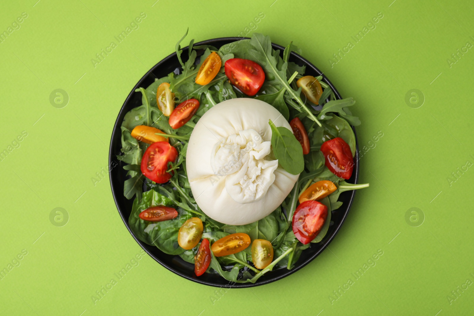 Photo of Delicious burrata salad on green table, top view