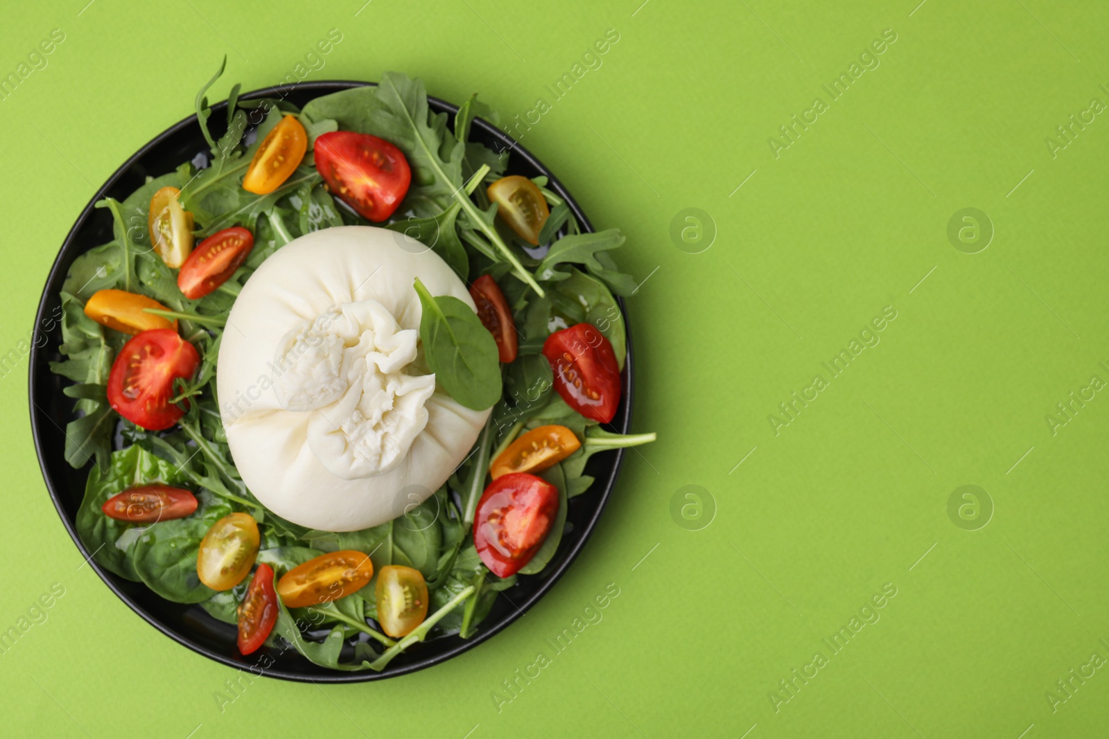 Photo of Delicious burrata salad on green table, top view. Space for text