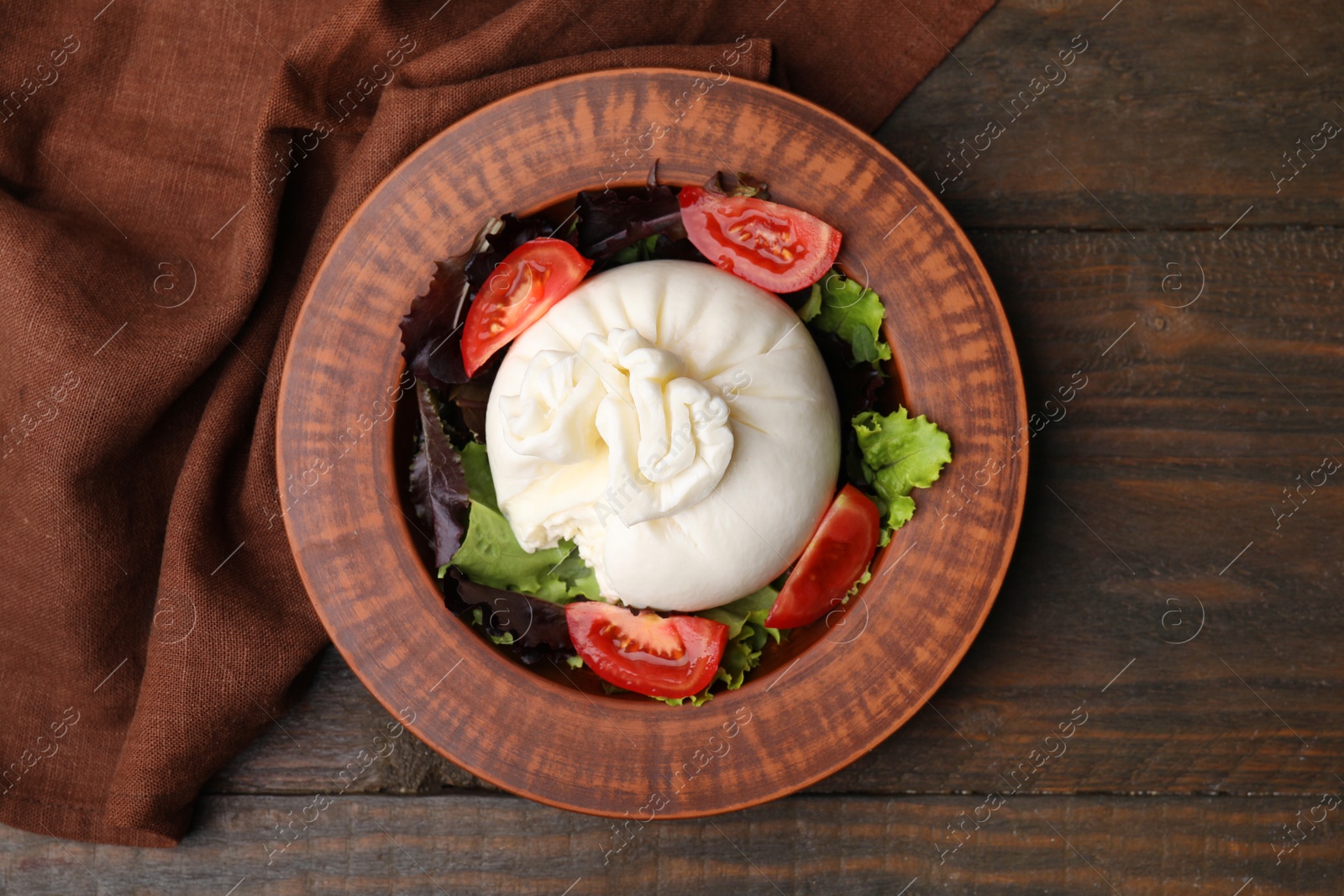 Photo of Delicious burrata salad in bowl on wooden table, top view