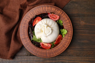 Photo of Delicious burrata salad in bowl on wooden table, top view