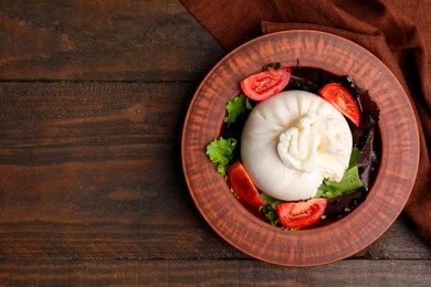 Photo of Delicious burrata salad in bowl on wooden table, top view. Space for text