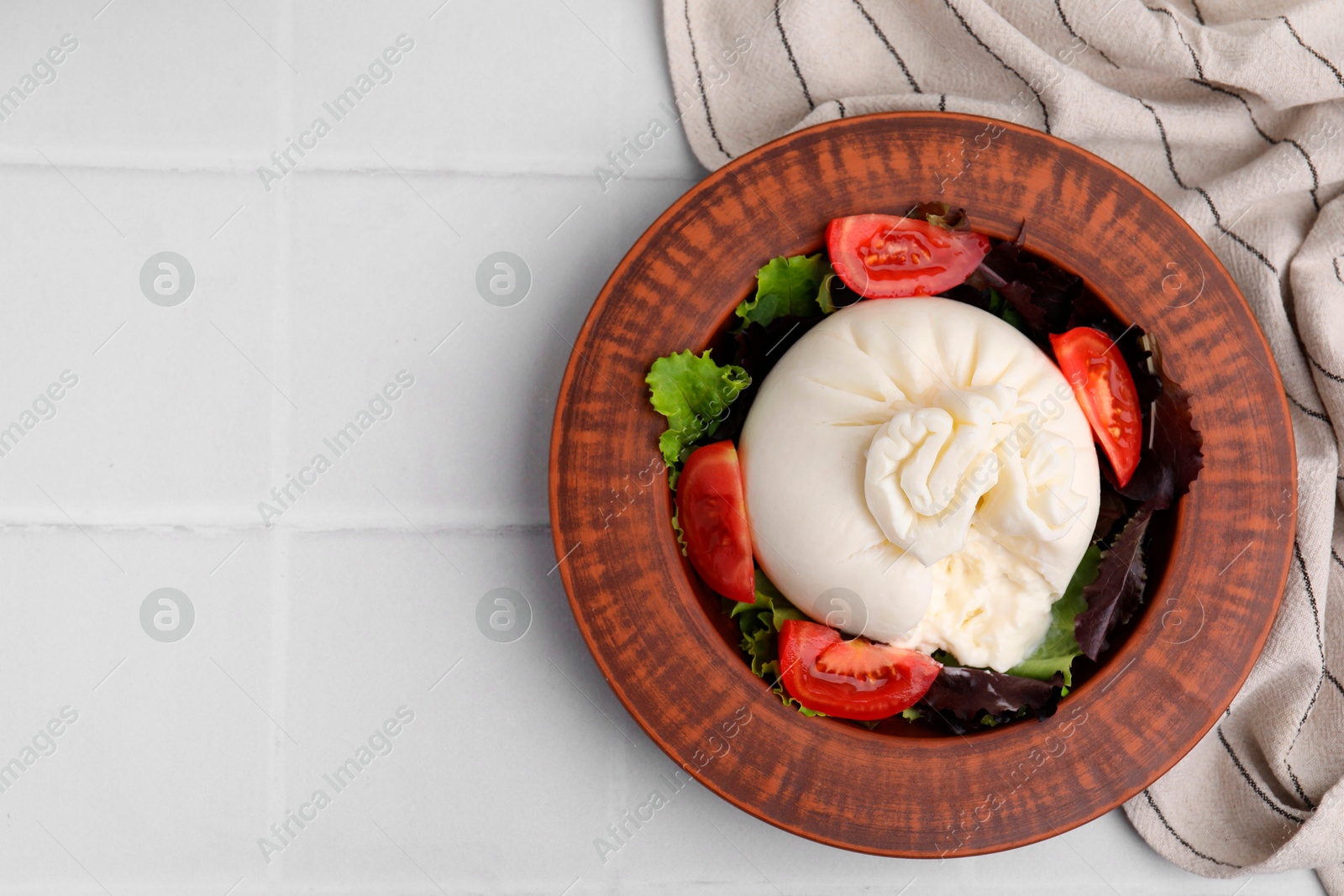 Photo of Delicious burrata salad in bowl on white tiled table, top view. Space for text