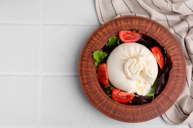 Photo of Delicious burrata salad in bowl on white tiled table, top view. Space for text