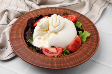 Photo of Delicious burrata salad in bowl on white tiled table, closeup