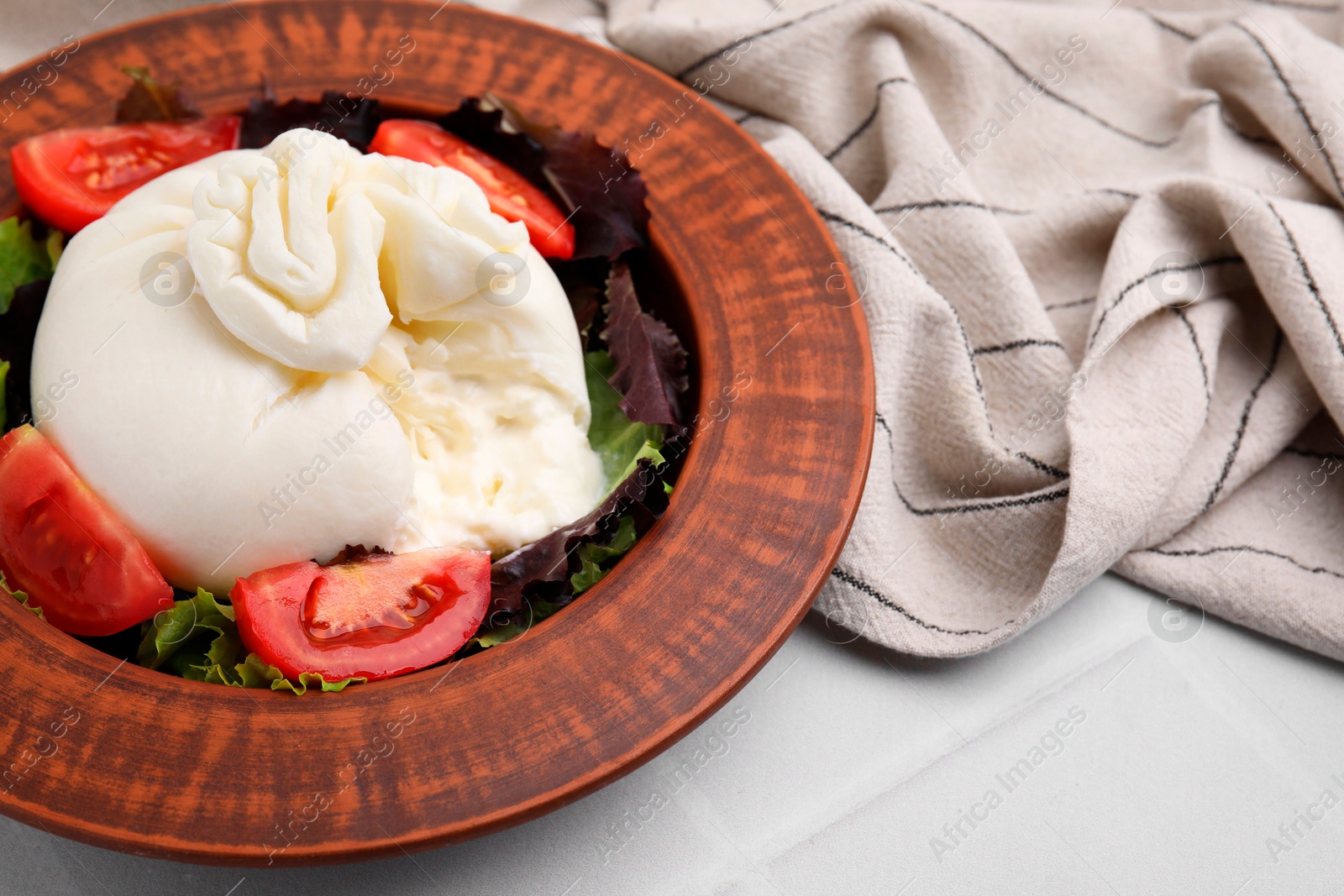 Photo of Delicious burrata salad in bowl on white tiled table, closeup