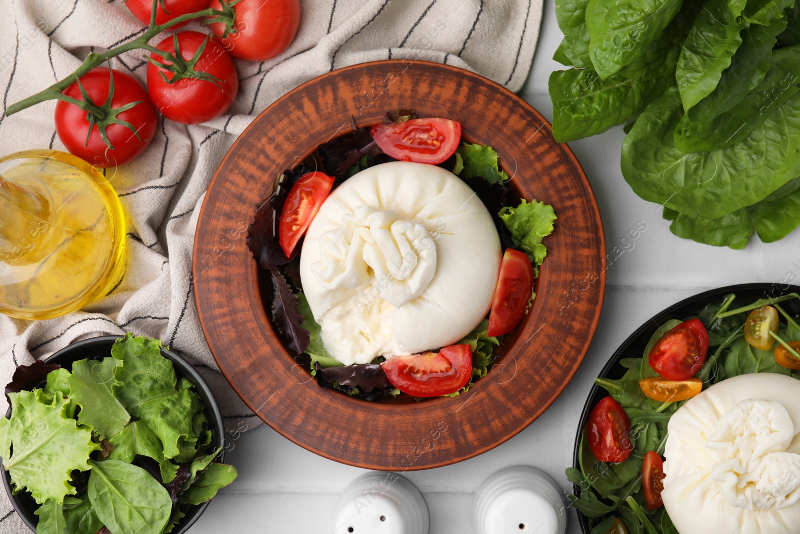 Photo of Delicious burrata salads in dishware on white tiled table, flat lay