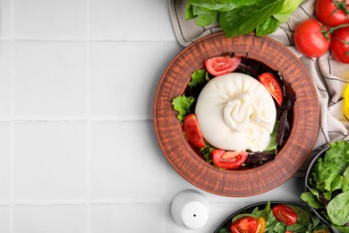 Photo of Delicious burrata salads in dishware on white tiled table, flat lay. Space for text