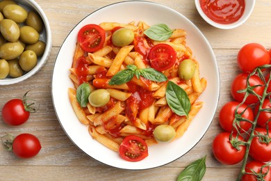 Photo of Delicious pasta with tomato sauce, basil and olives in bowl on wooden table, flat lay