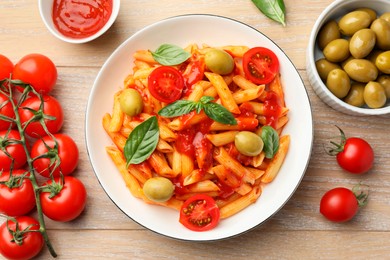 Delicious pasta with tomato sauce, basil and olives in bowl on wooden table, flat lay