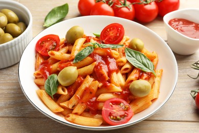 Photo of Delicious pasta with tomato sauce, basil and olives in bowl on wooden table, closeup