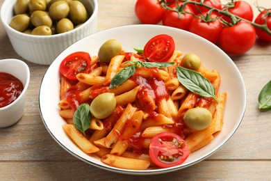 Photo of Delicious pasta with tomato sauce, basil and olives in bowl on wooden table, closeup