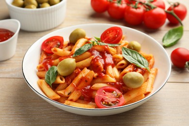 Photo of Delicious pasta with tomato sauce, basil and olives in bowl on wooden table, closeup