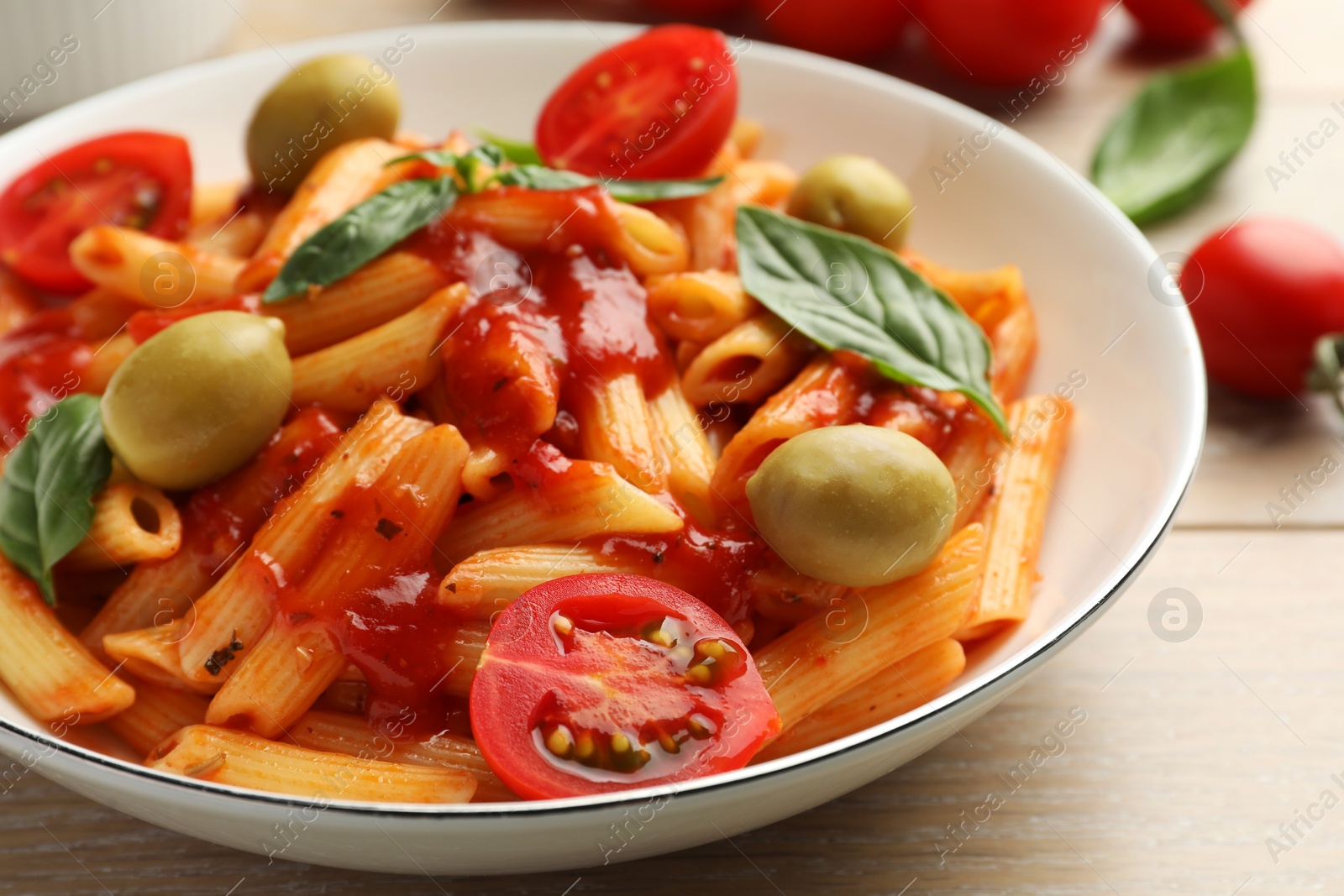 Photo of Delicious pasta with tomato sauce, basil and olives in bowl on wooden table, closeup