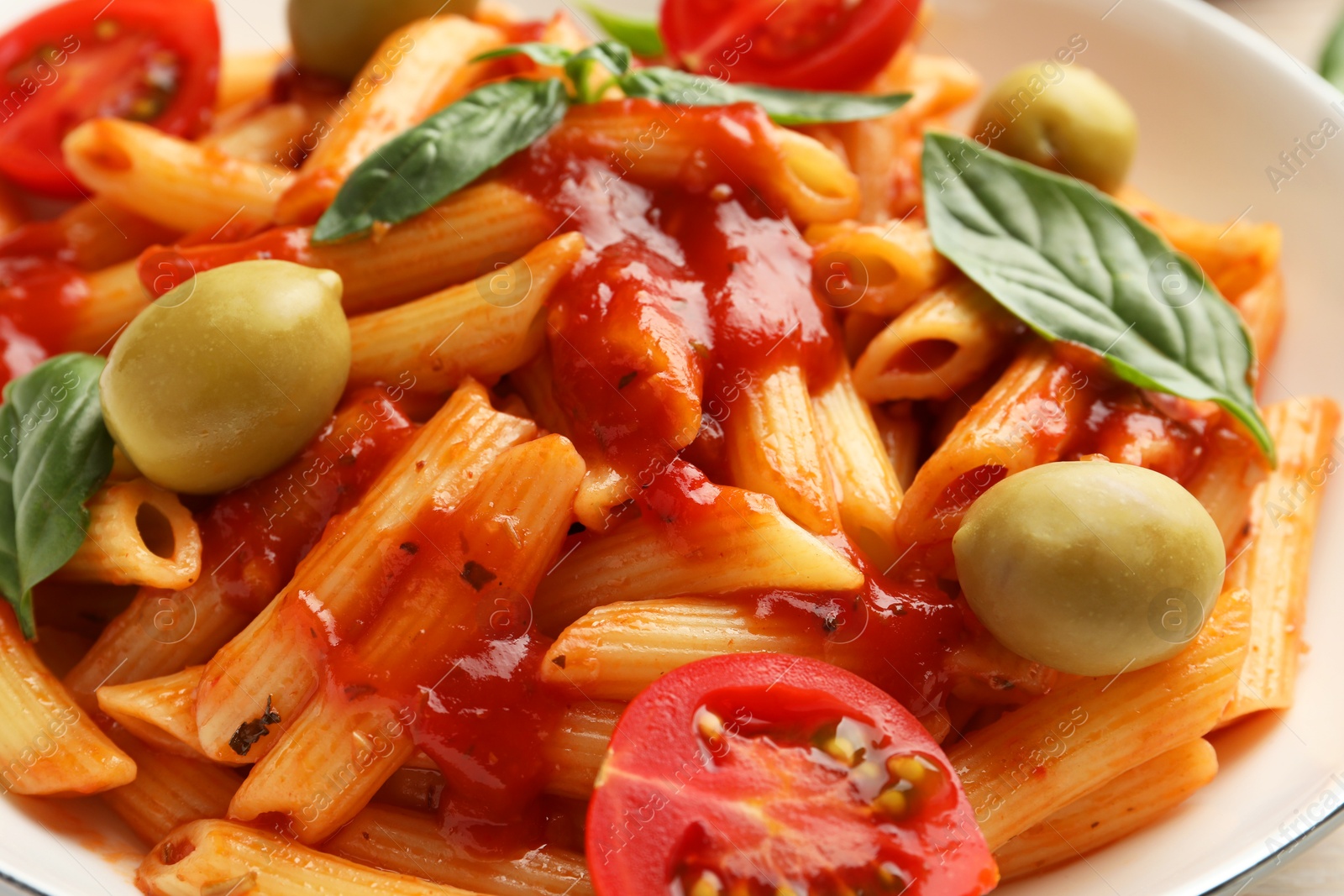 Photo of Delicious pasta with tomato sauce, basil and olives in bowl, closeup