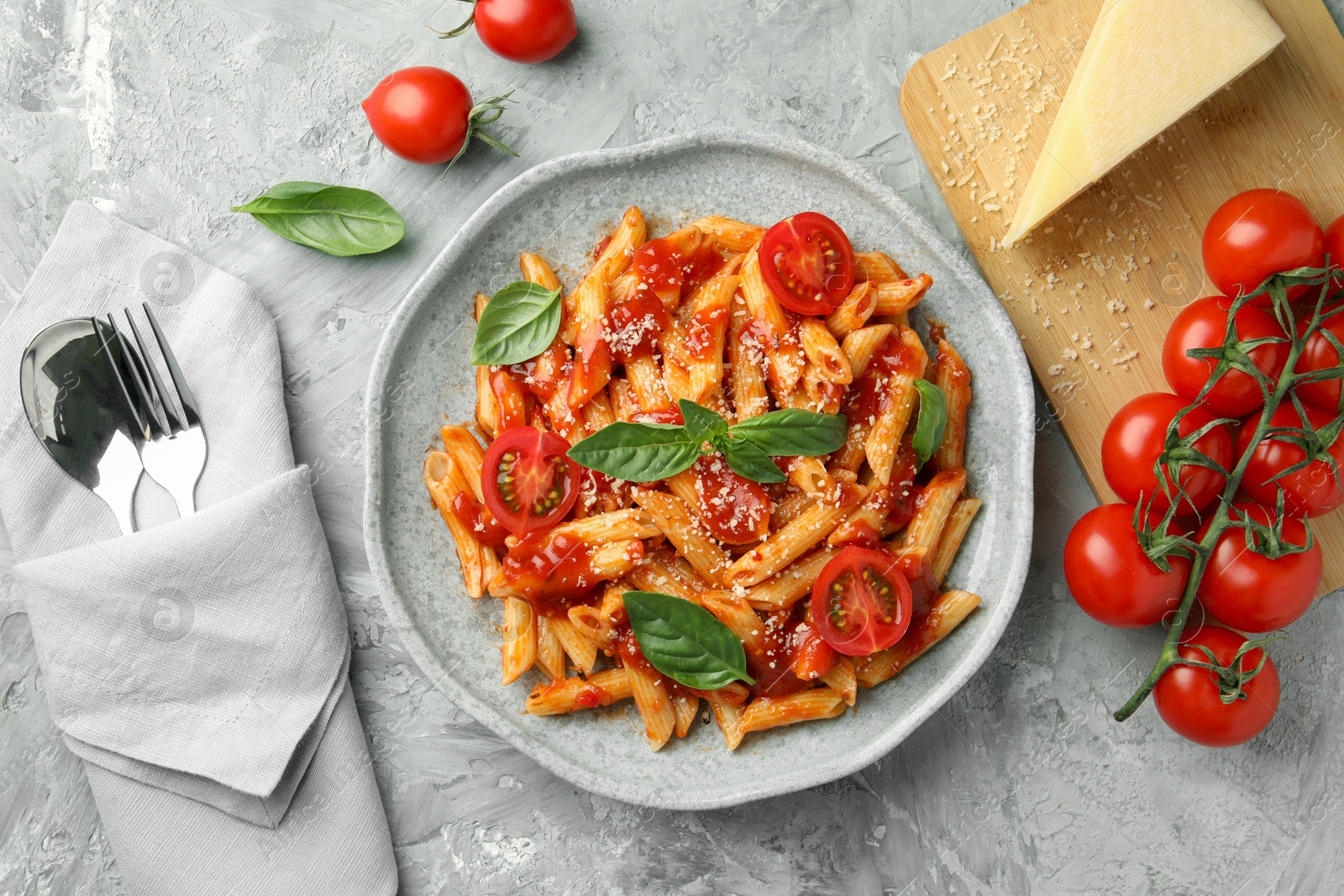 Photo of Delicious pasta with tomato sauce, basil and cheese on served gray textured table, flat lay