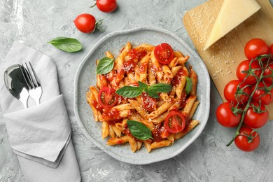 Photo of Delicious pasta with tomato sauce, basil and cheese on served gray textured table, flat lay