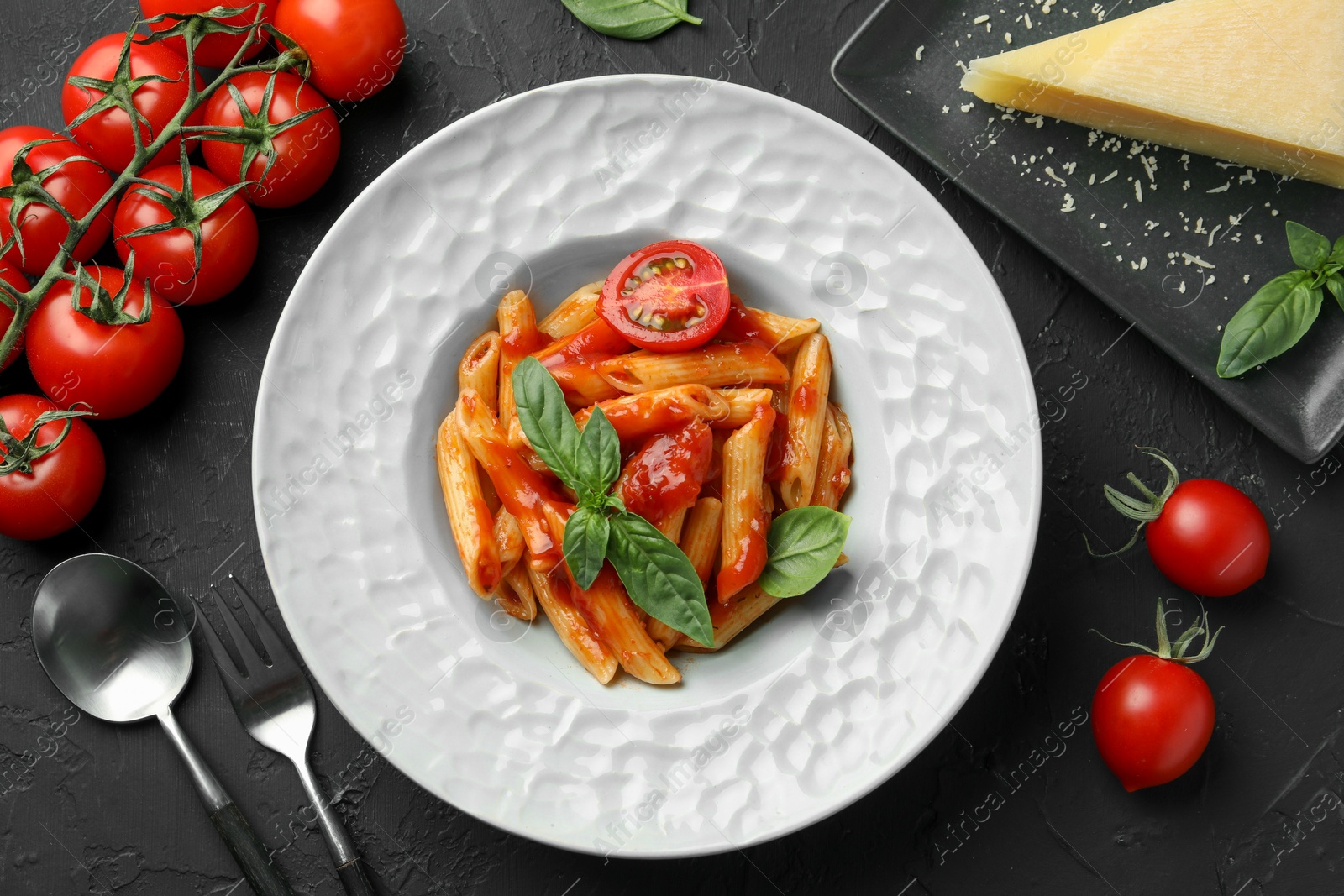 Photo of Delicious pasta with tomato sauce, basil and cheese served on black textured table, flat lay