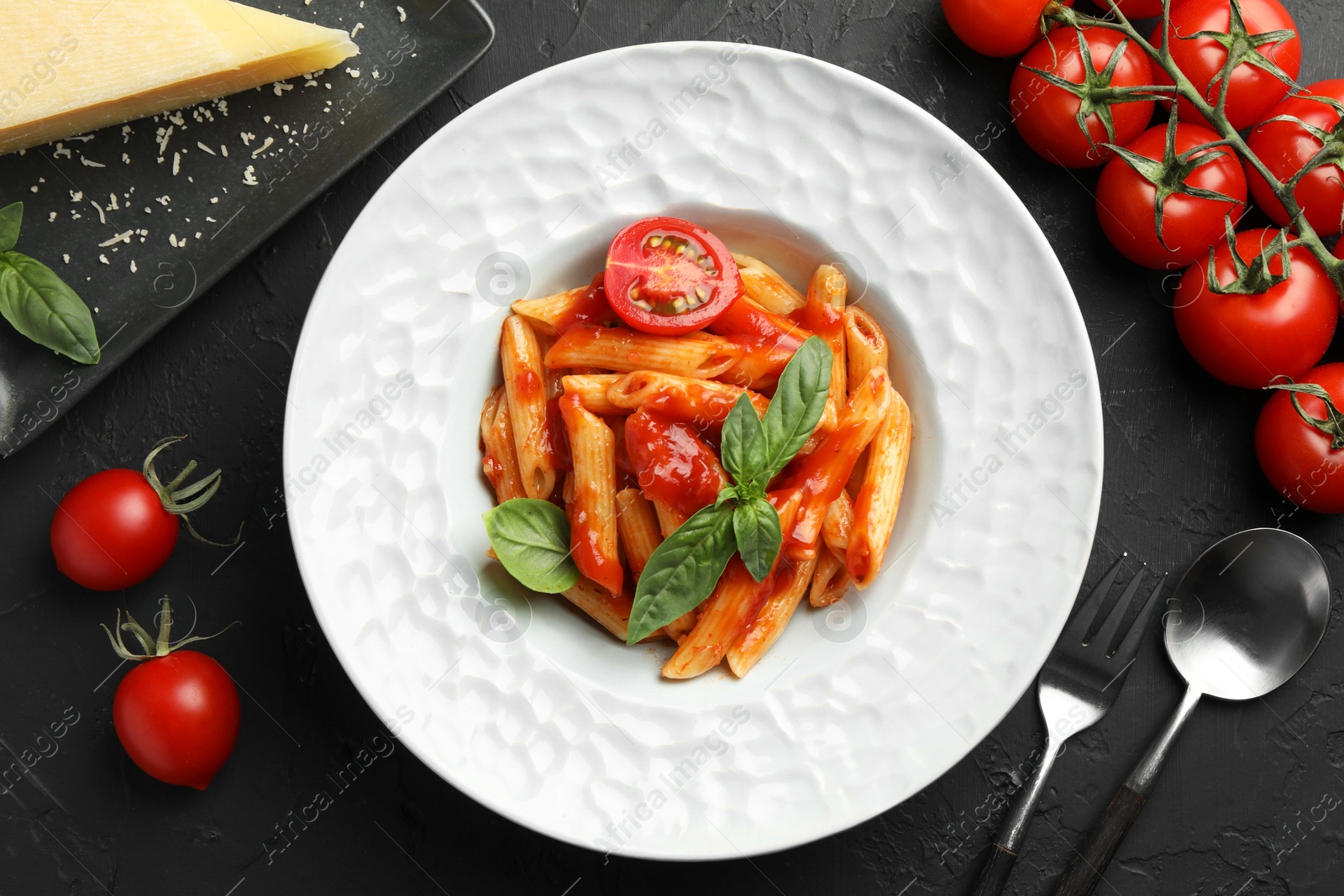 Photo of Delicious pasta with tomato sauce, basil and cheese served on black textured table, flat lay