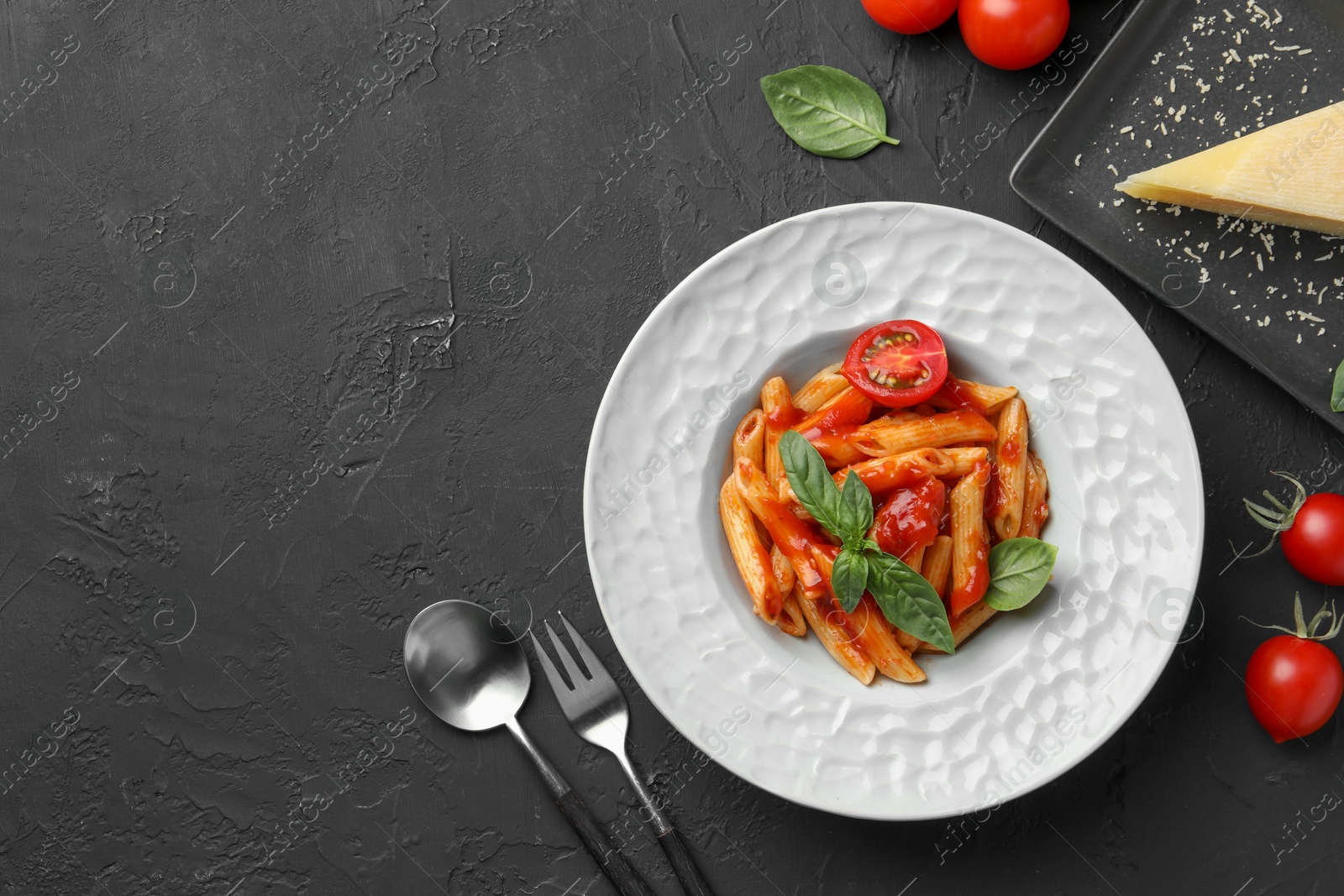 Photo of Delicious pasta with tomato sauce, basil and cheese served on black textured table, flat lay. Space for text