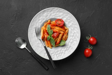 Photo of Delicious pasta with tomato sauce and basil served on black textured table, flat lay