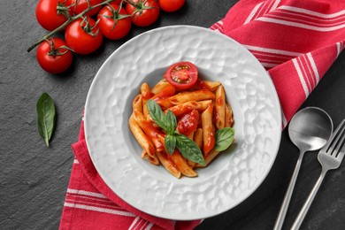 Delicious pasta with tomato sauce and basil served on black textured table, flat lay