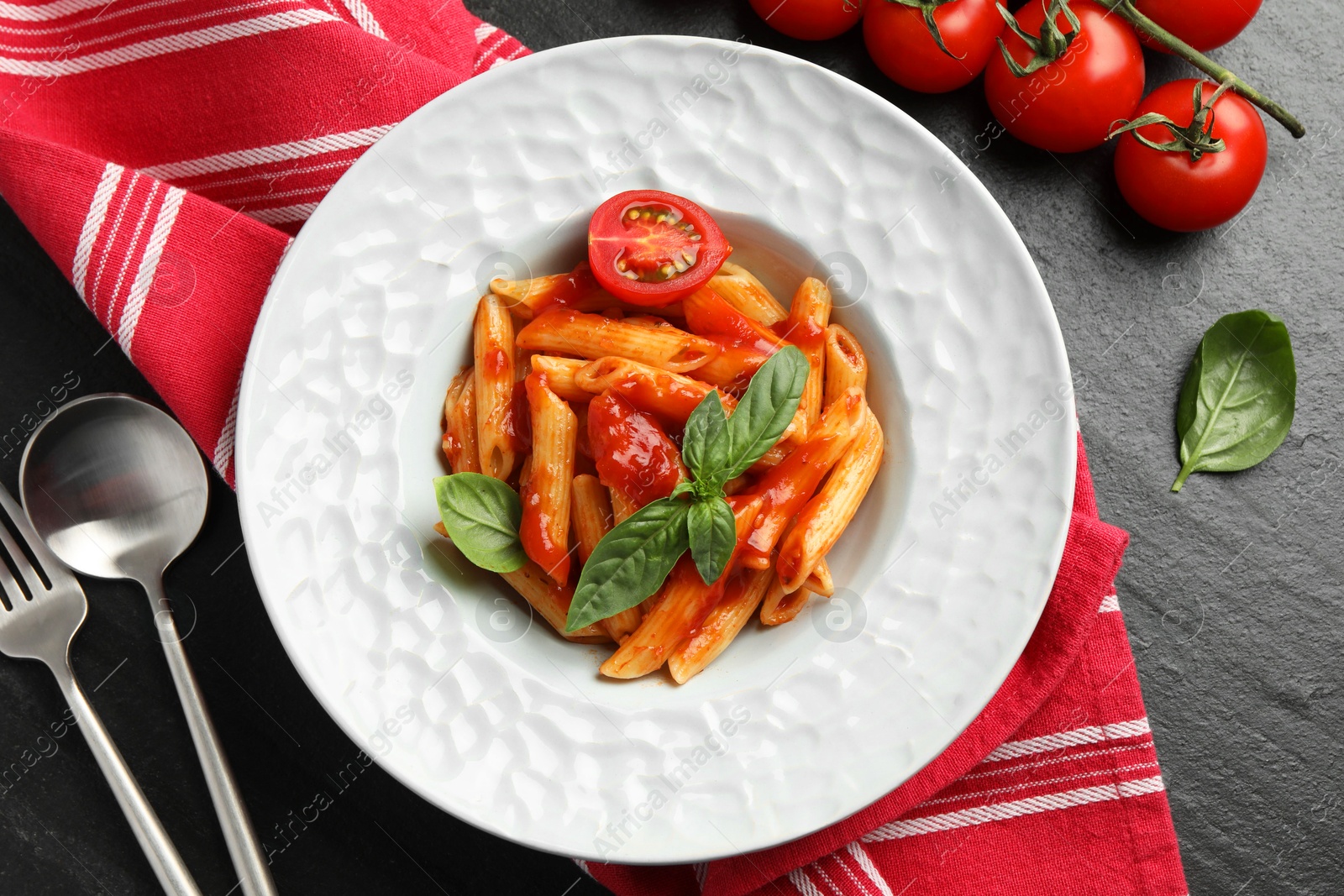 Photo of Delicious pasta with tomato sauce and basil served on black textured table, flat lay