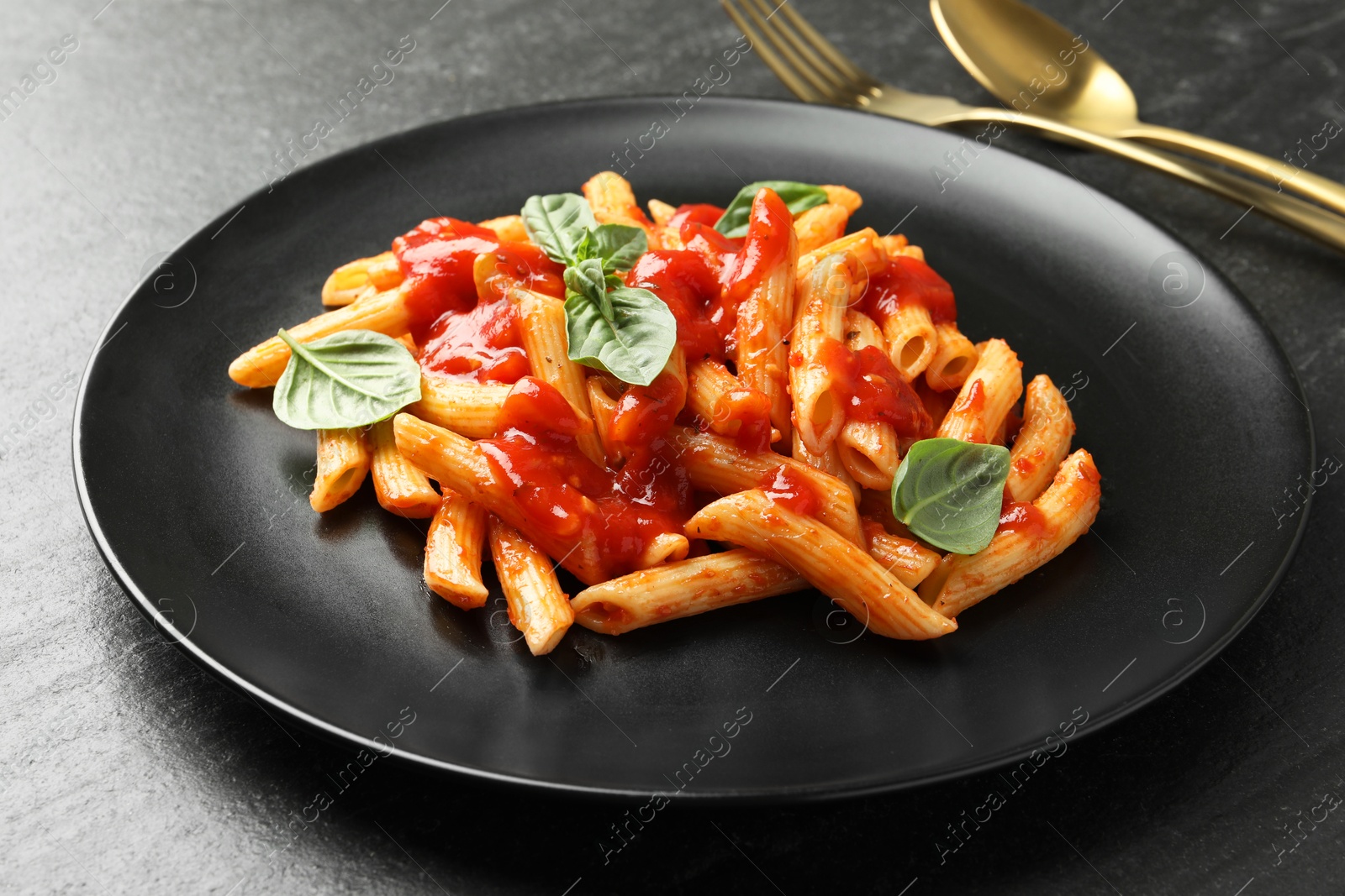 Photo of Delicious pasta with tomato sauce and basil served on black textured table, closeup