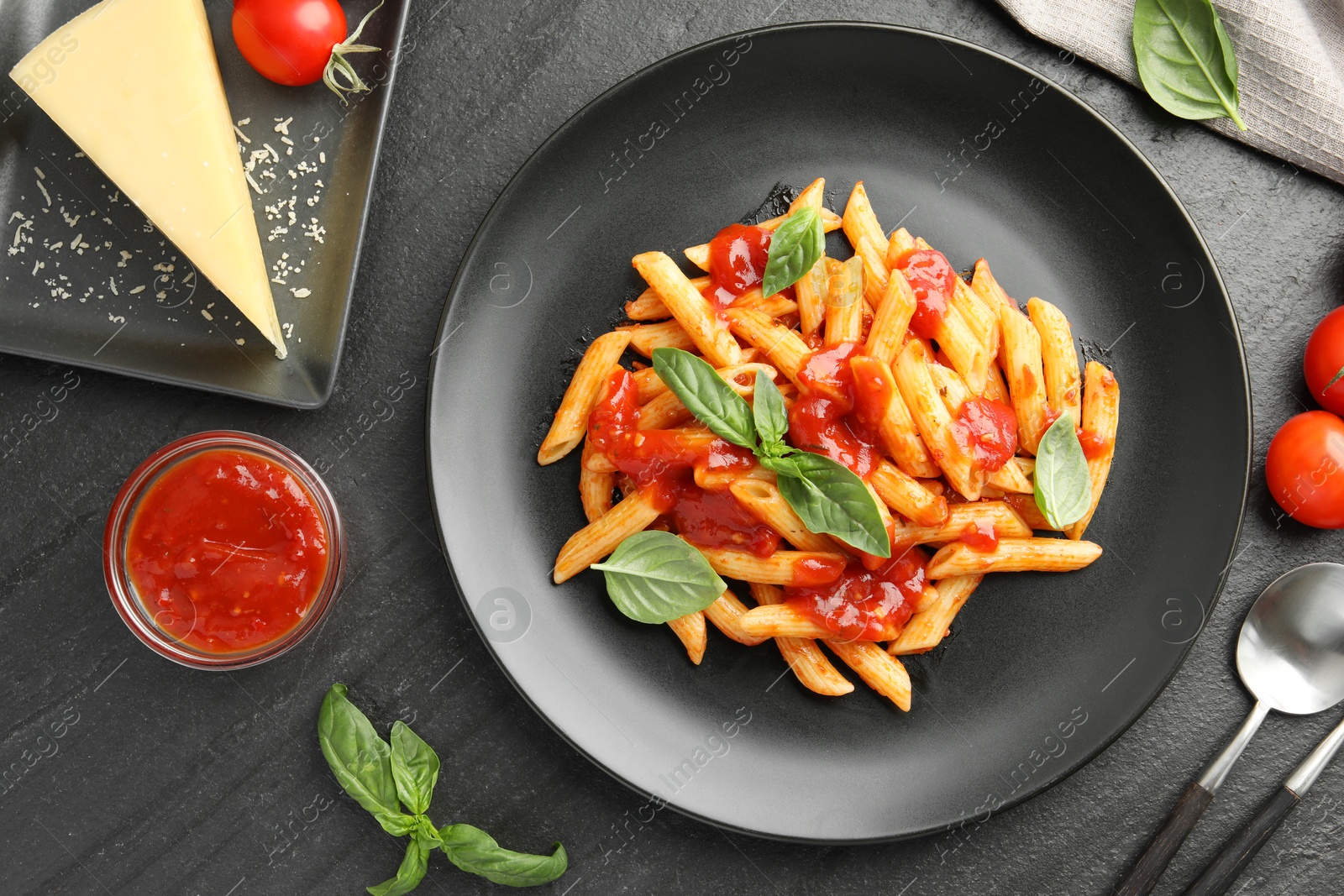 Photo of Delicious pasta with tomato sauce, basil and cheese served on black textured table, flat lay