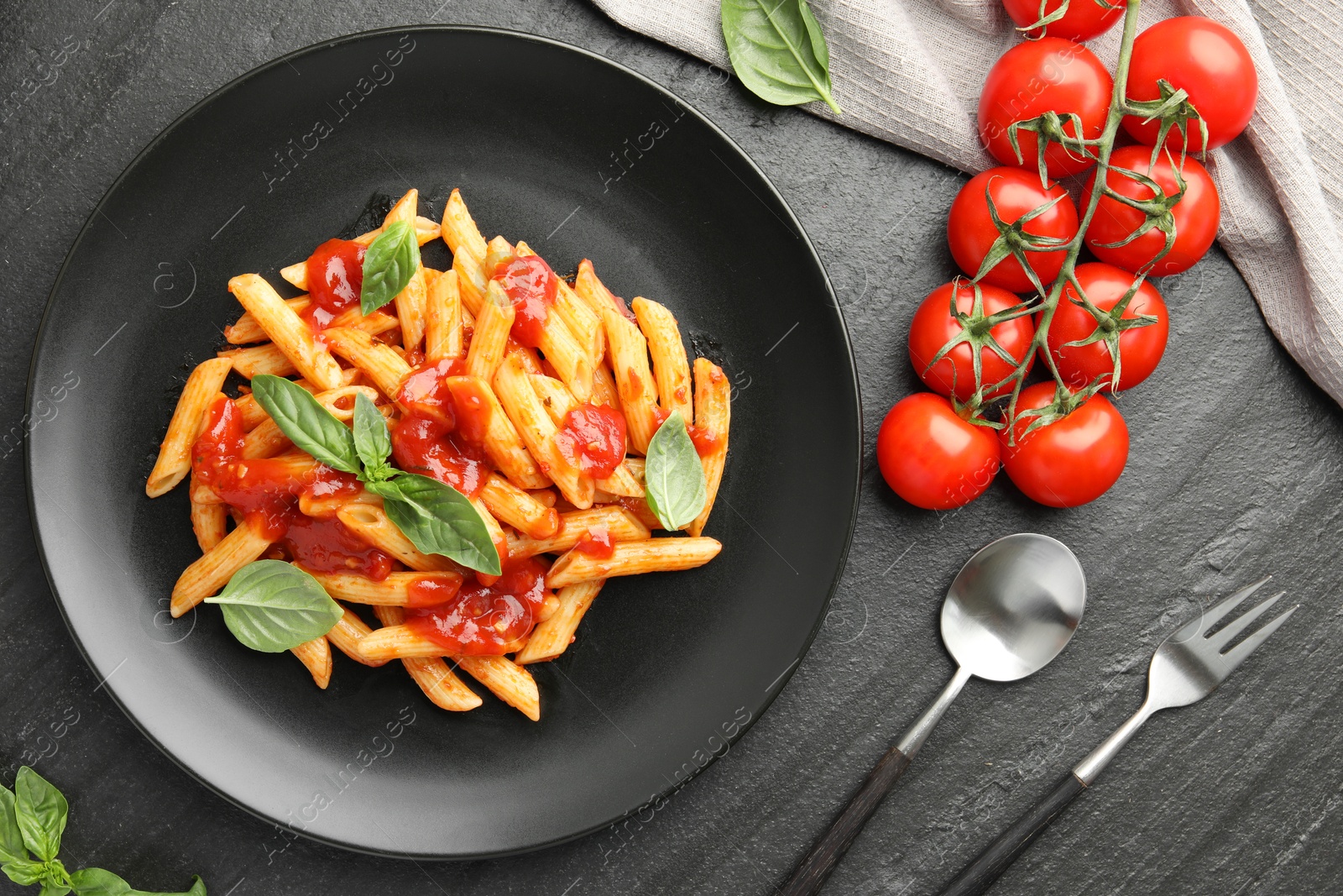 Photo of Delicious pasta with tomato sauce and basil served on black textured table, flat lay