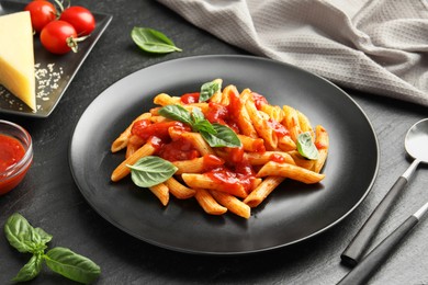 Photo of Delicious pasta with tomato sauce, basil and cheese served on black textured table, closeup