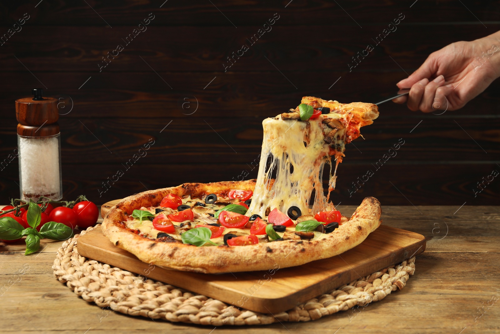 Photo of Woman taking piece of tasty pizza with melted cheese at wooden table, closeup