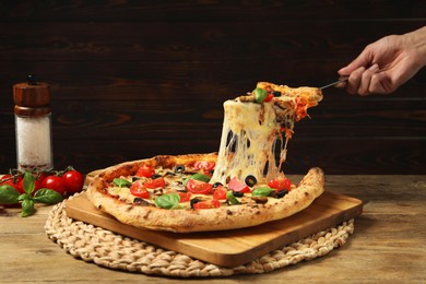 Woman taking piece of tasty pizza with melted cheese at wooden table, closeup