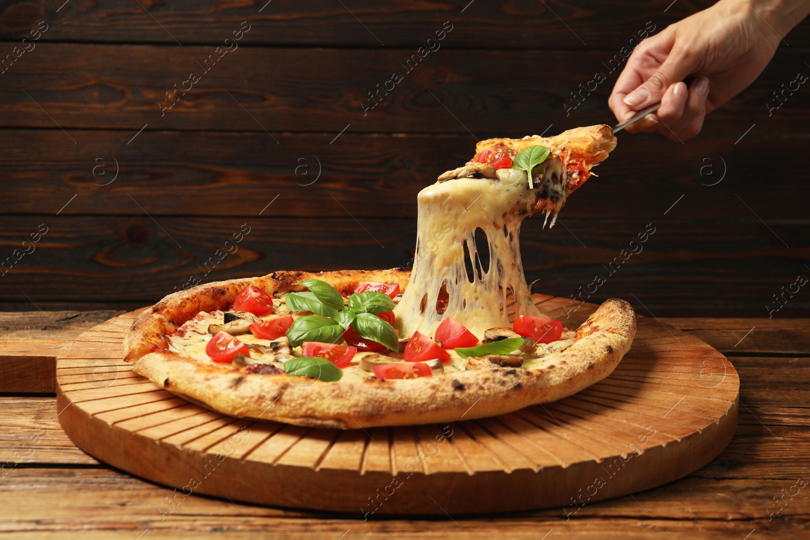 Photo of Woman taking piece of tasty pizza with melted cheese at wooden table, closeup