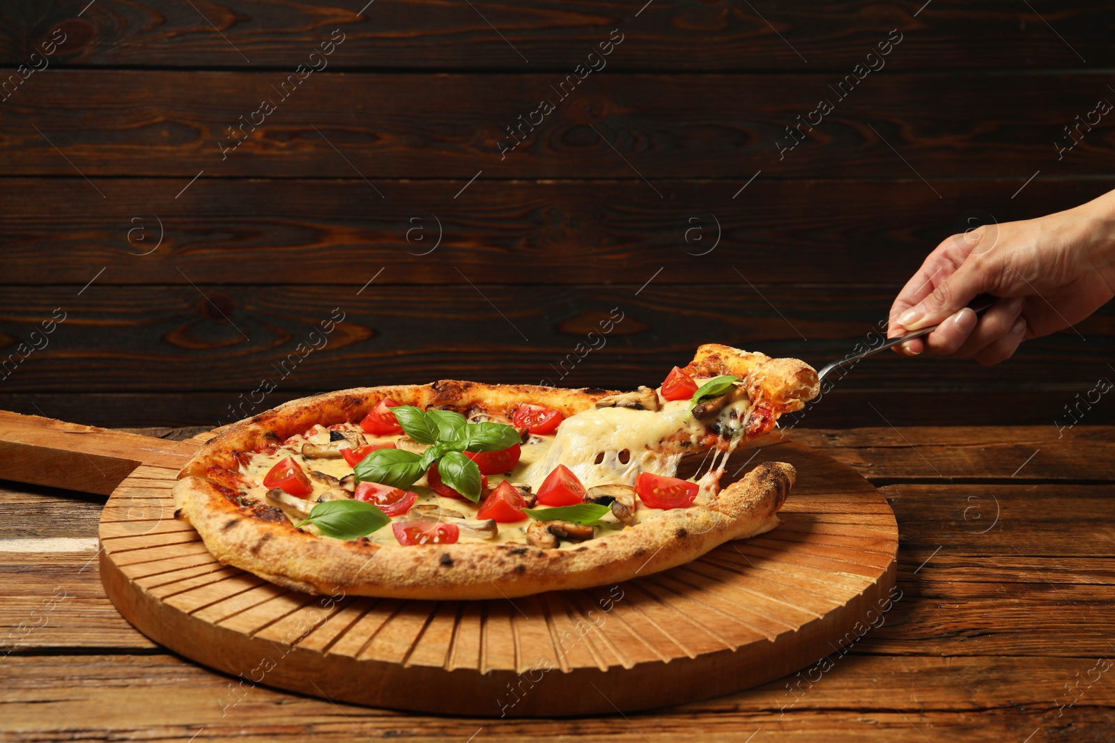 Photo of Woman taking piece of tasty pizza with melted cheese at wooden table, closeup