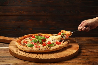 Woman taking piece of tasty pizza with melted cheese at wooden table, closeup